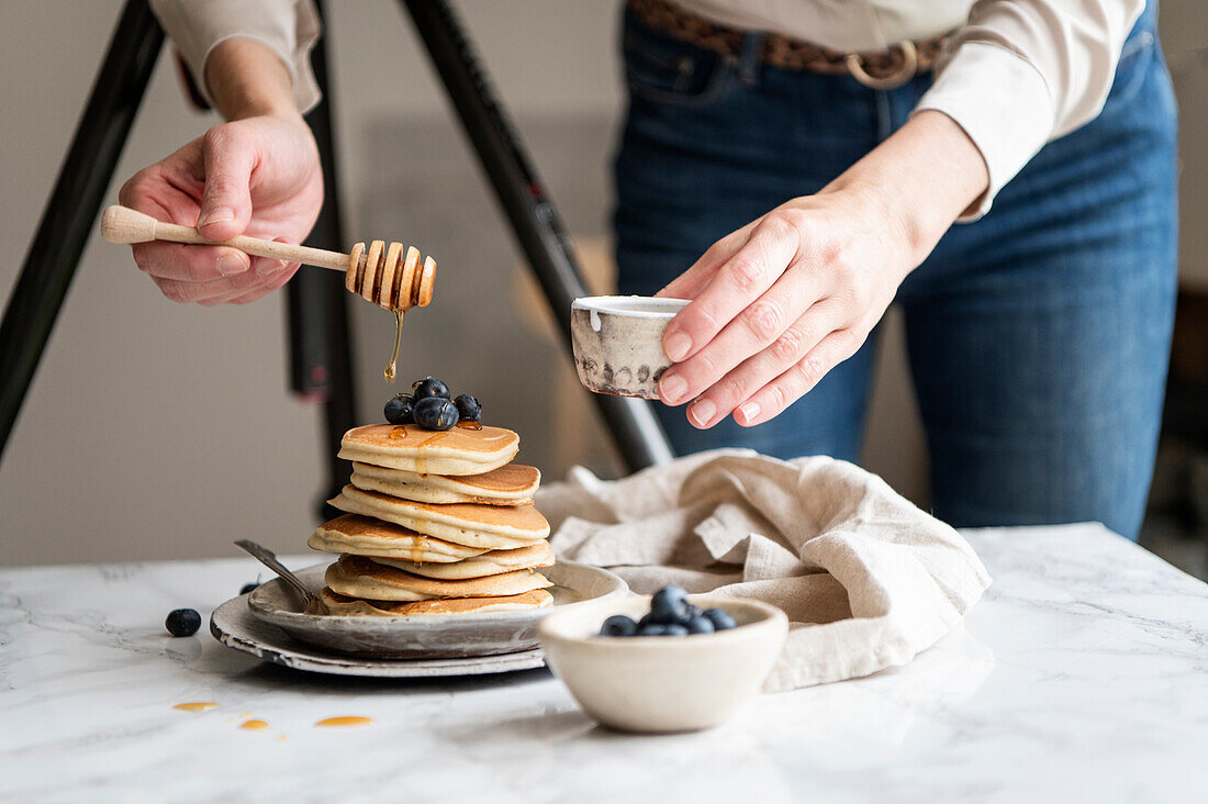 Frauenhände beträufeln Pancakes und Blaubeeren mit Honig