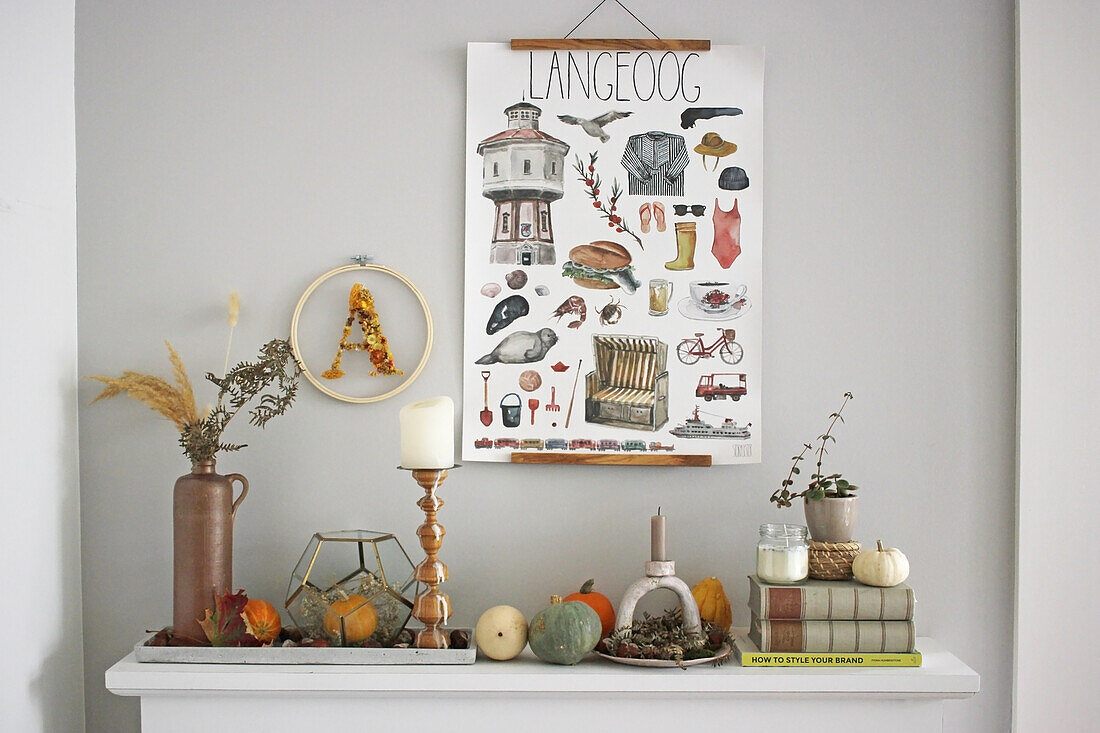 Autumnal decoration with ornamental pumpkins on a mantelpiece, with an illustrated poster hanging from above