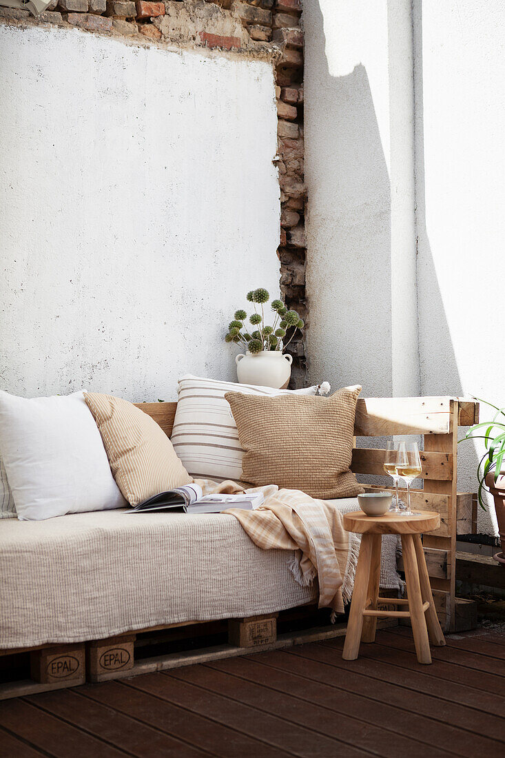 Cosy sofa with scatter cushions, blanket and book with bouquet of dried globe thistles in background on terrace