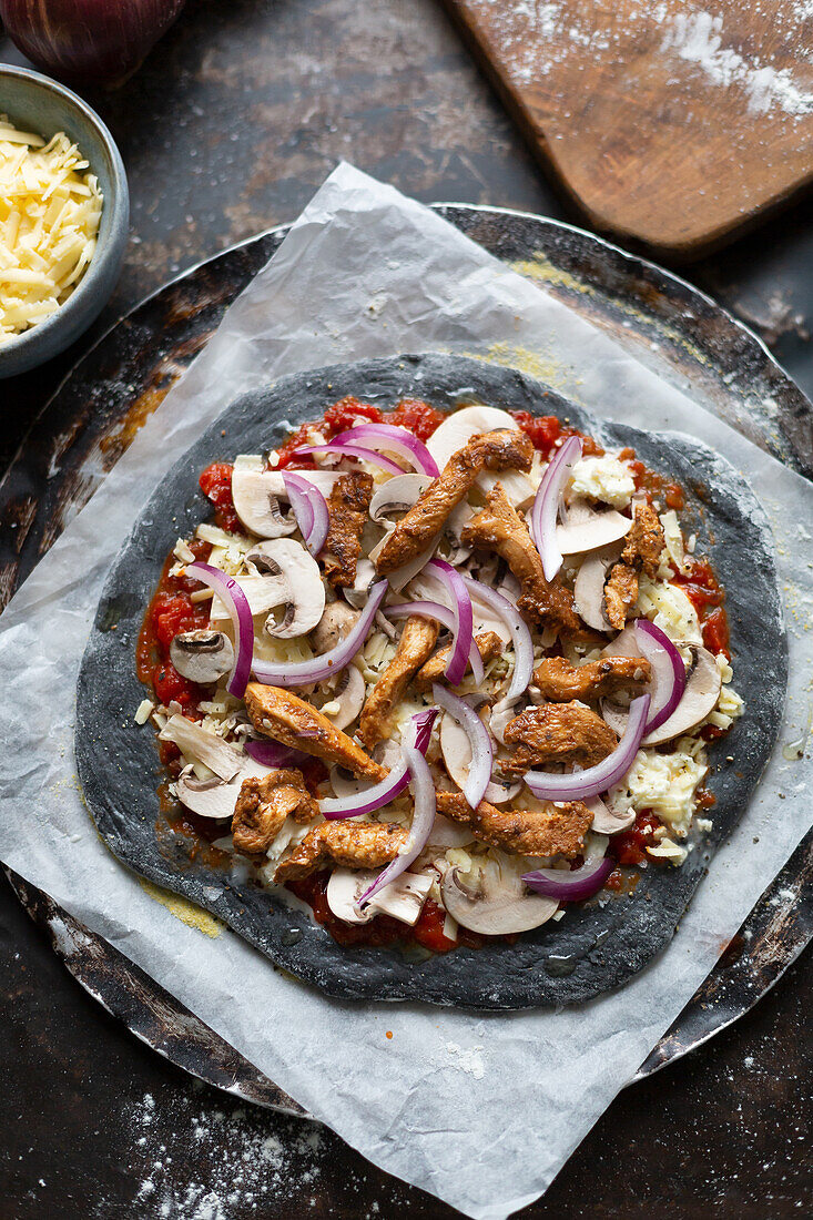 Preparing black pizza with grilled chicken, mushrooms and red onions