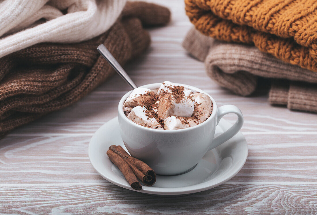 Hot chocolate with marshmallow and pile of warm knitted clothes