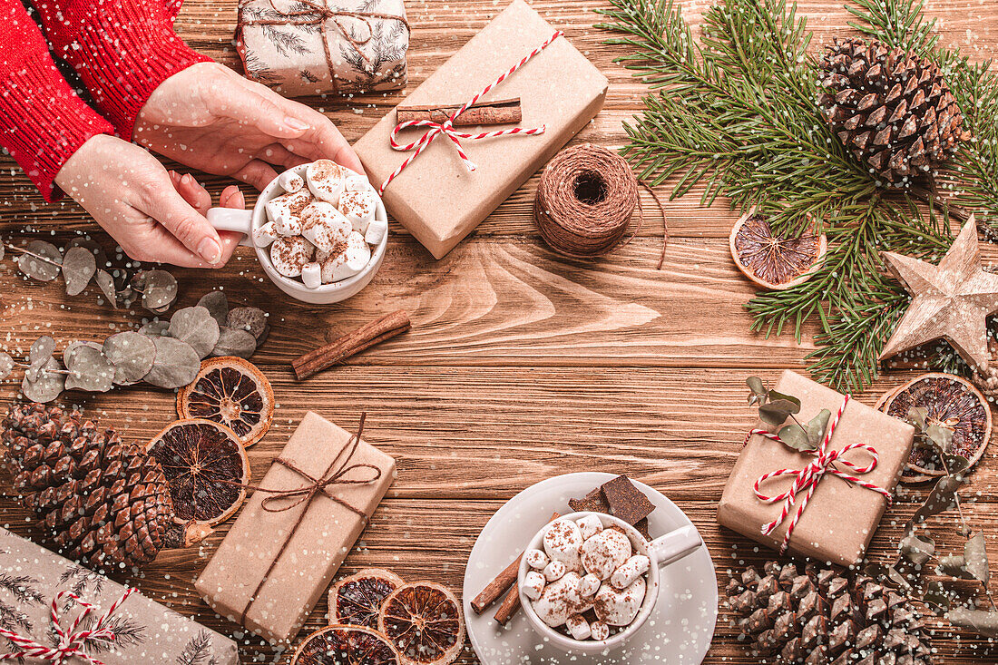 Female hands holding a cup of marshmallow cacao, wrapped presents