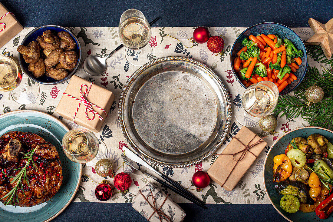 Weihnachtstisch mit festlichen Gerichten (Schweinshaxe und Gemüse) und Vintage Metallplatte