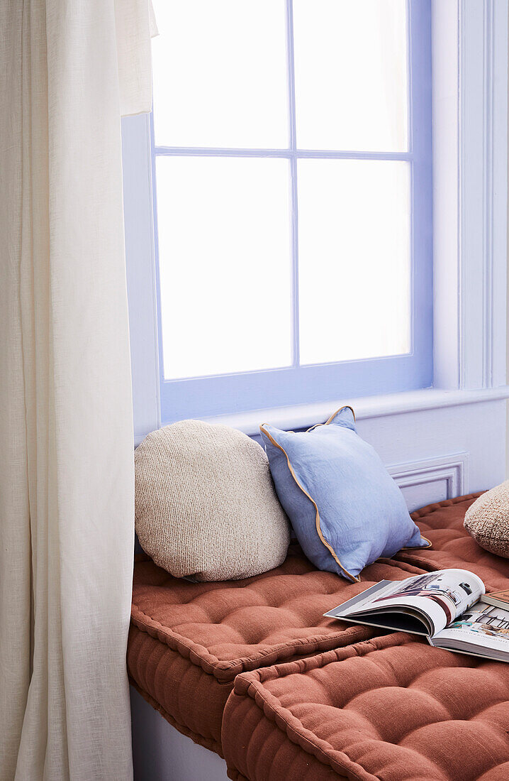 Terracotta-colored cushions on a bench in front of a window