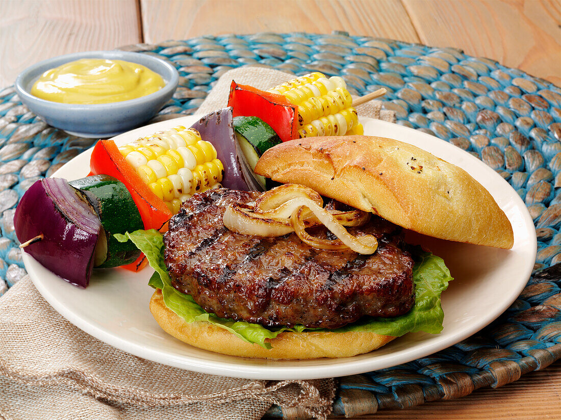 Grilled ground pork burger with grilled onions on a ciabatta bun and vegetable skewer