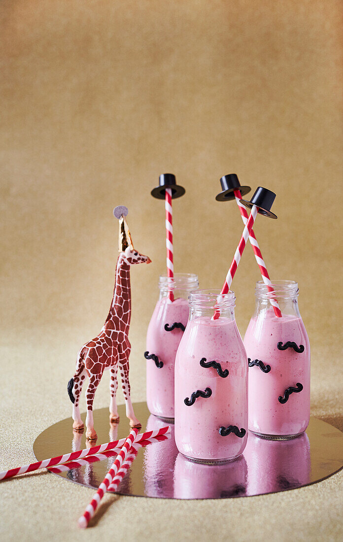 Raspberry smoothie in bottles, straws with top hats, and giraffe figure