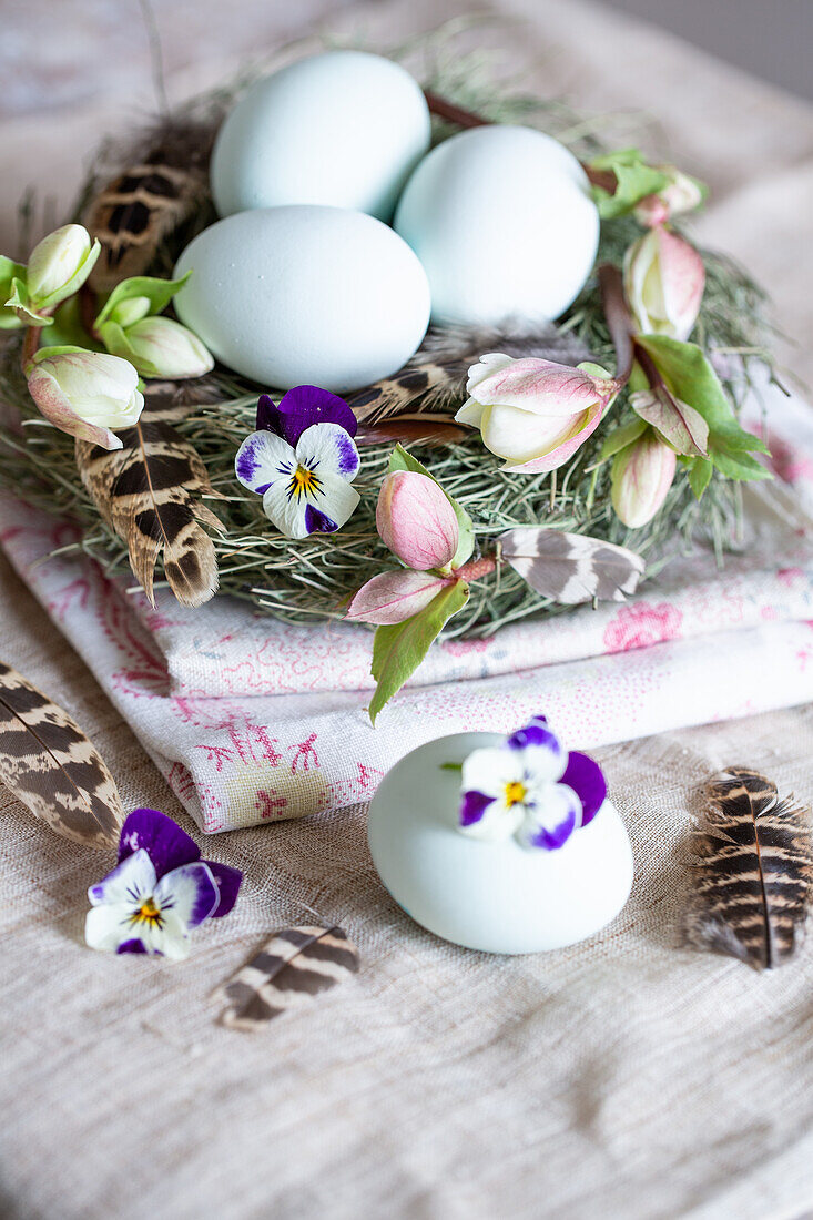 Ostereier mit Blüten und Federn in einem Nest auf Stoff