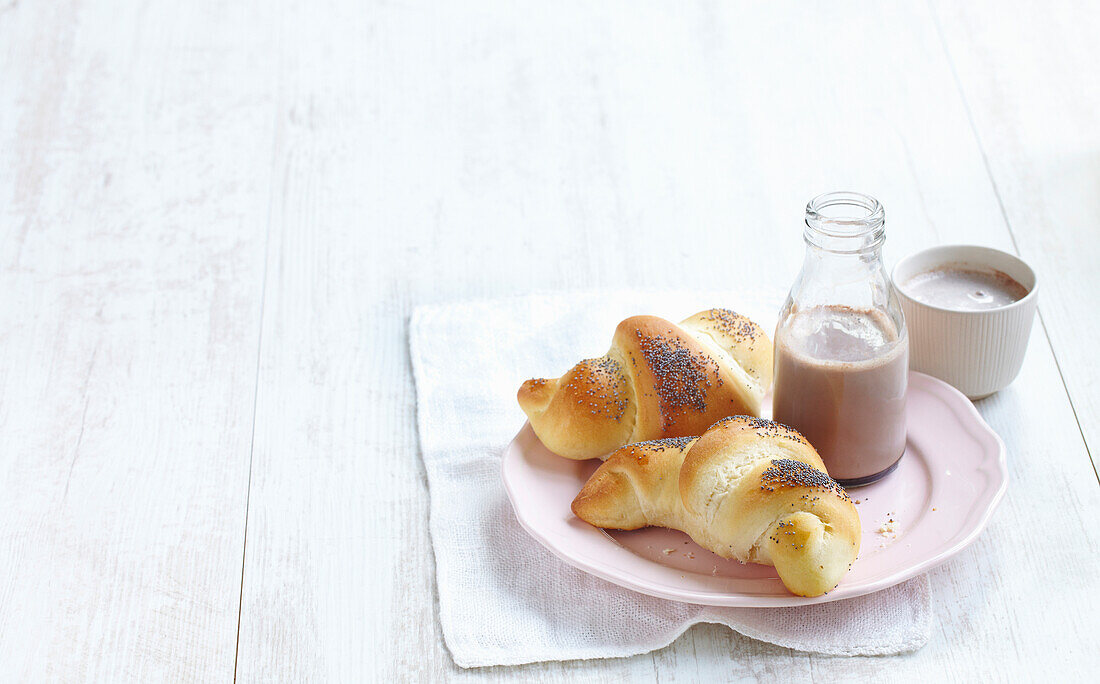 Croissants with poppy seeds served with cocoa in a glass bottle and a cup