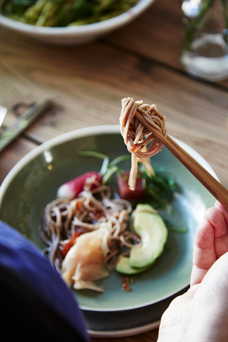 A woman eating a poke bowl with buckwheat noodles and tuna