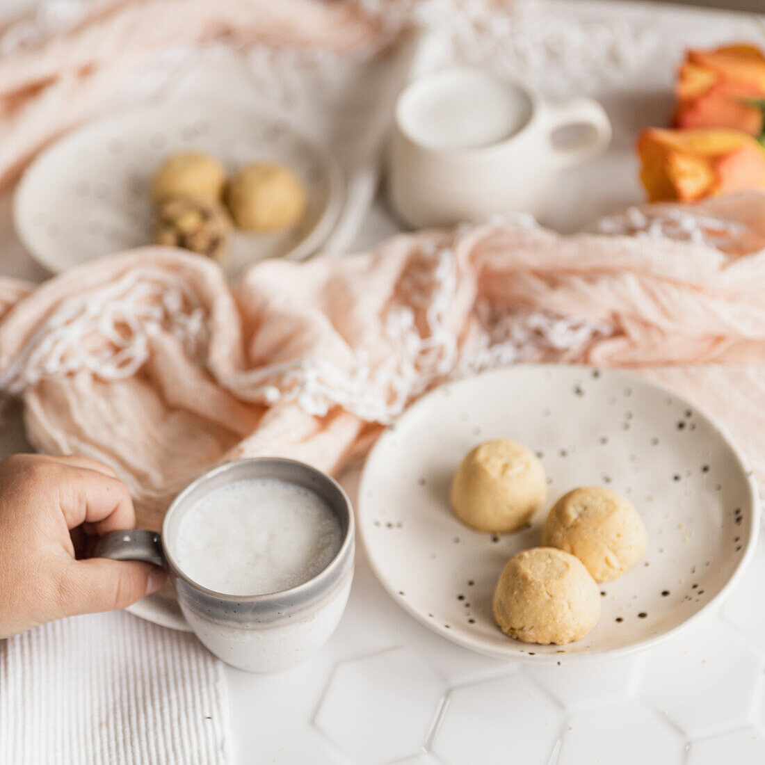 Childs hand holding a babychino in a stoneware espresso mug, with shortbreak cookies on white stoneware plates