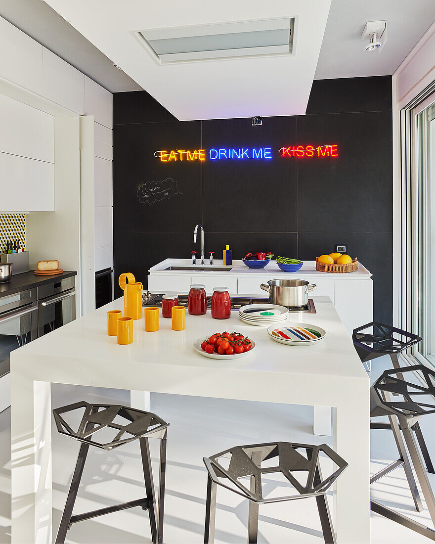 White table with designer stools and kitchen island in front of a black wall with a neon sign