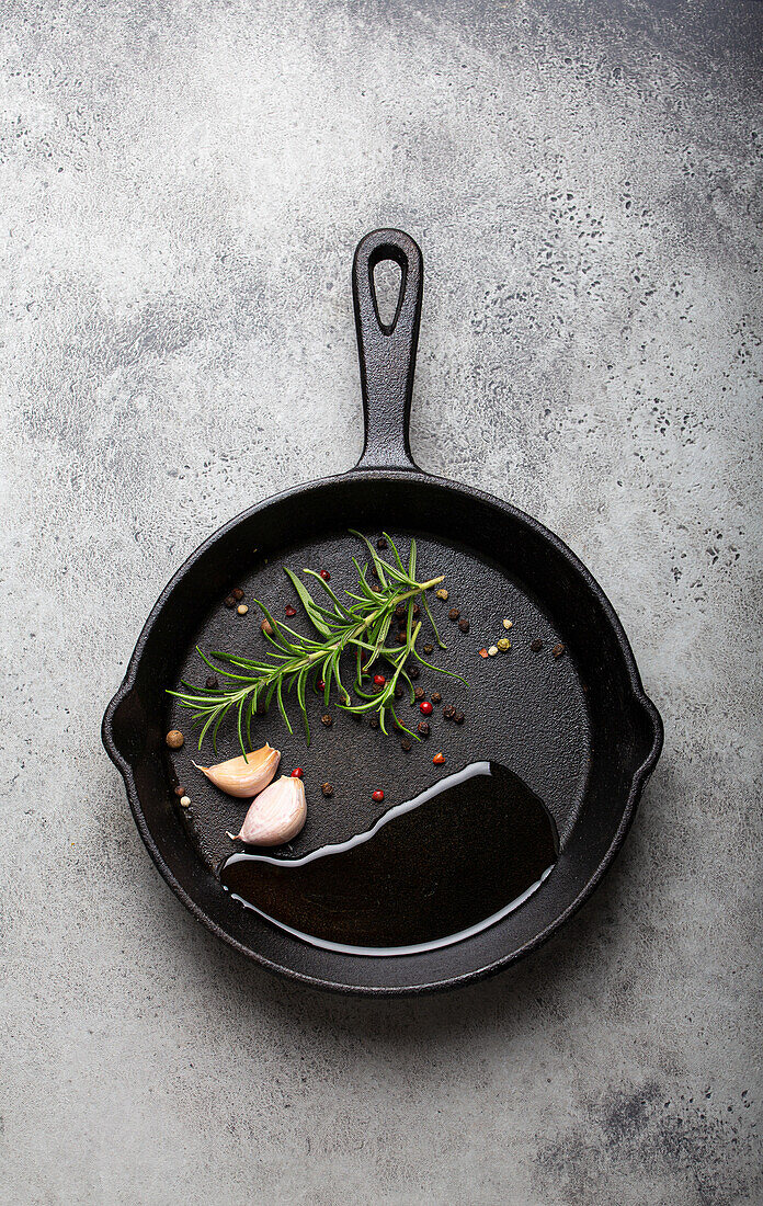 Schwarze Gusseisenpfanne mit Öl, Knoblauch, Pfeffer und Rosmarin