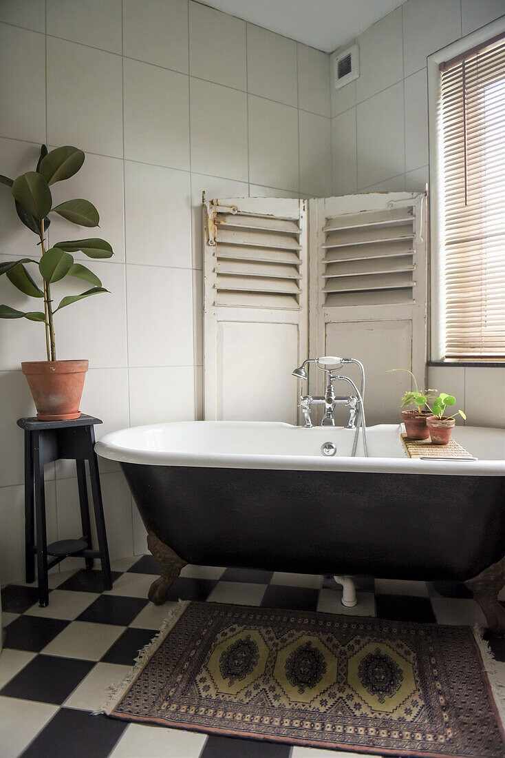 Vintage bathtub in front of screen in corner of bathroom with chequered tiles