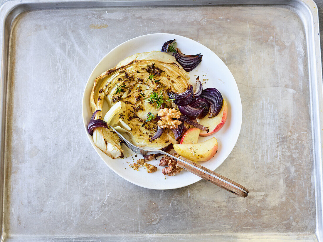 White cabbage steaks ona baking sheet with red onions and apples