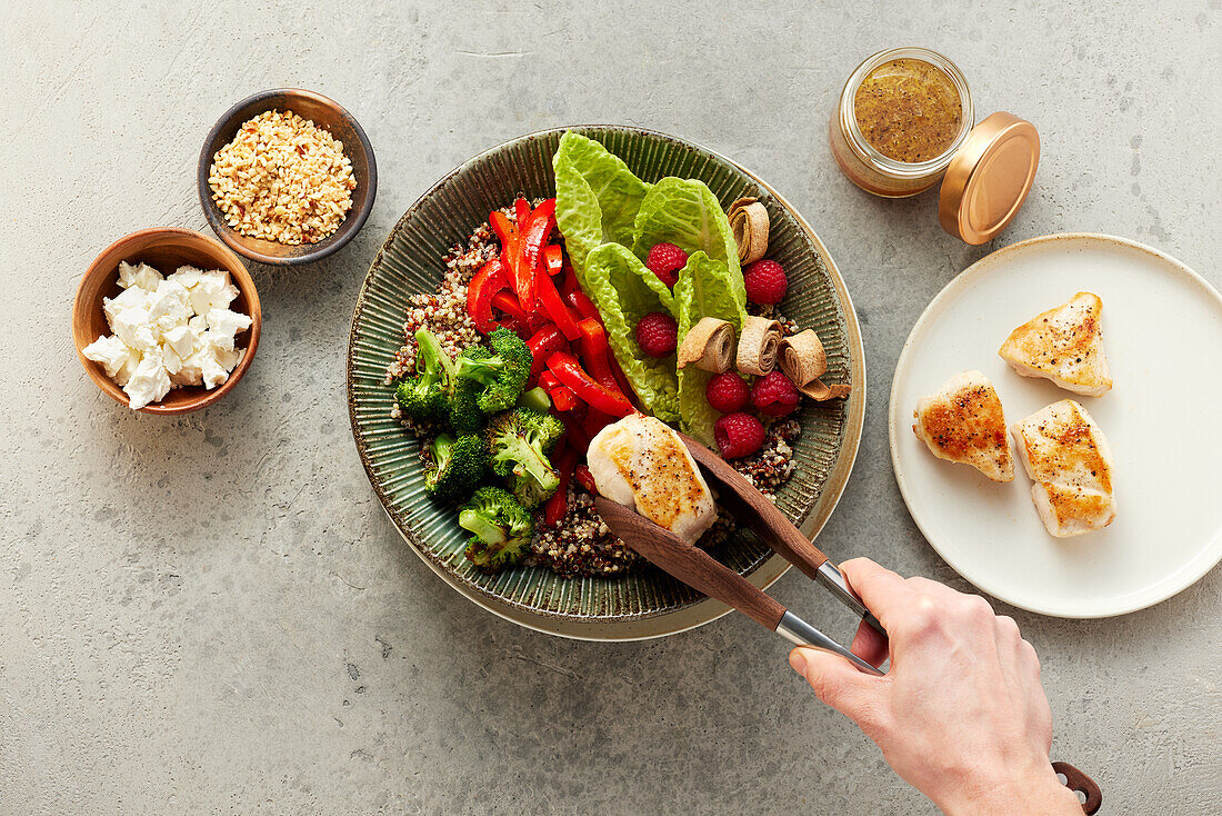 A bowl being arranged with quinoa, broccoli, peppers and chicken breast