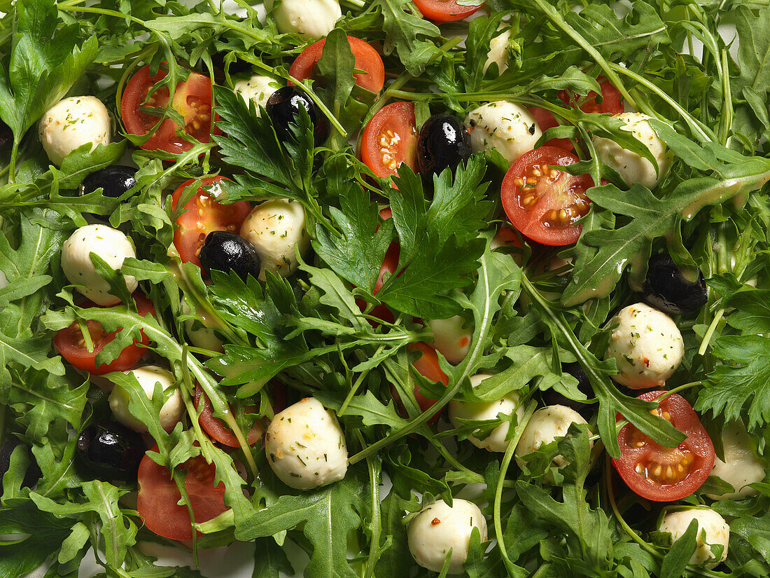 Rucolasalat mit Tomaten, Mozzarella und Oliven (bildfüllend)