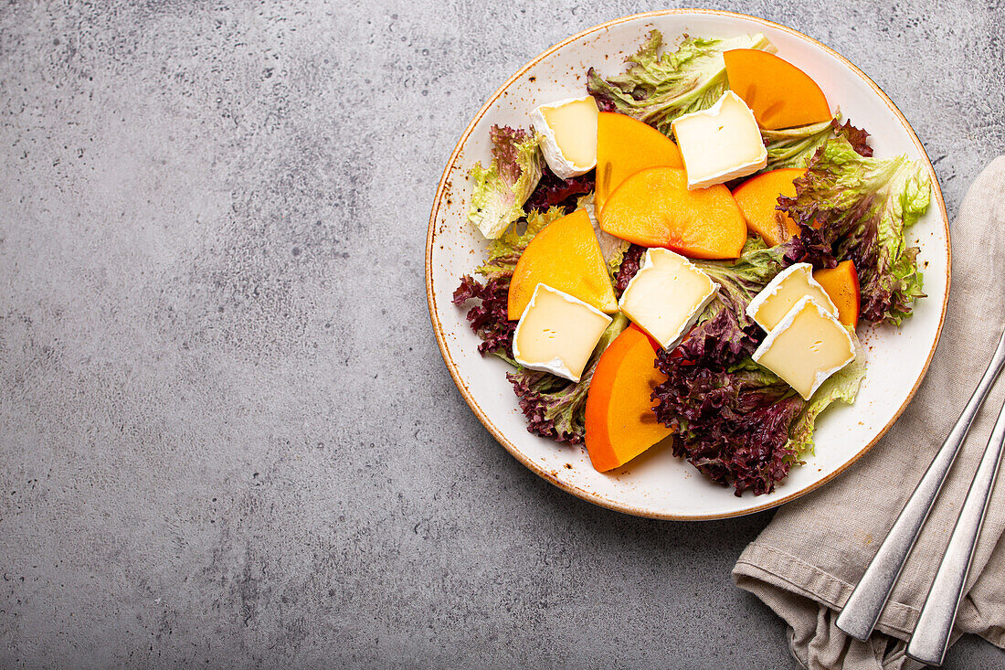 Persimmon salad with brie cheese and fresh salad leaves