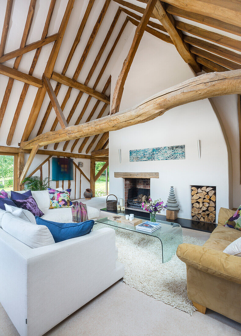 Sitzmöbel und Glas-Couchtisch vor Kamin in umgebauter Scheune mit Holzbalken