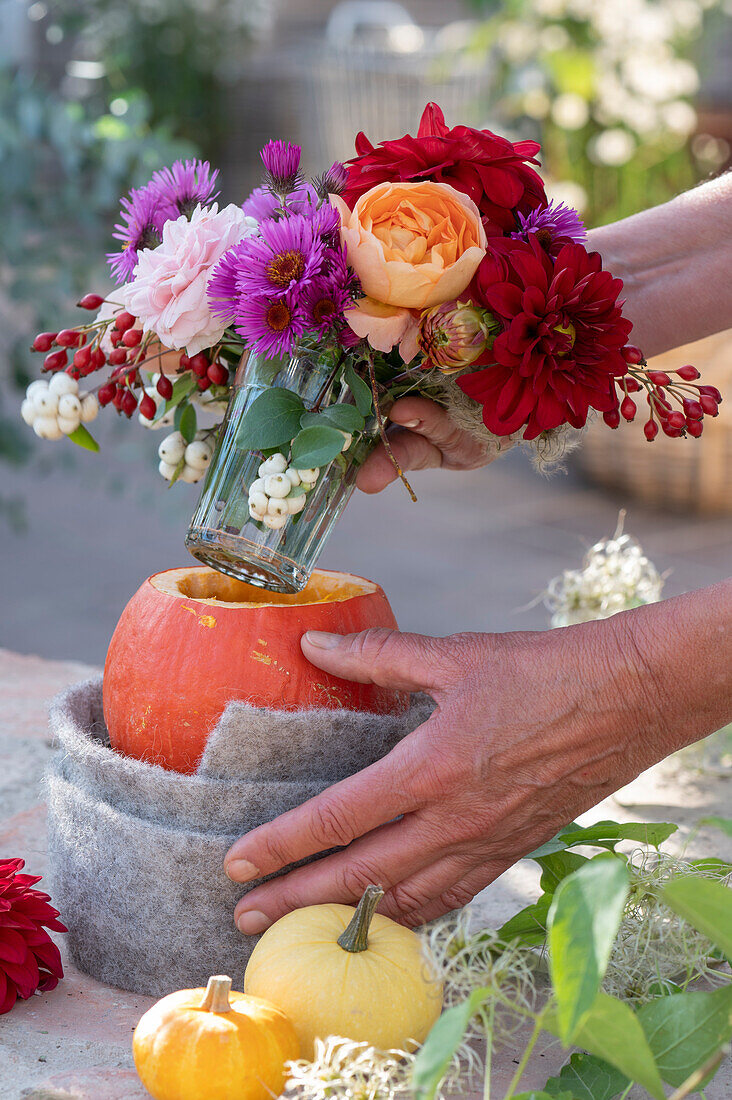 Autumn bouquet in pumpkin vase: Woman places bouquet of roses, dahlias, asters, snowberries and rose hips in glass in hollowed pumpkin