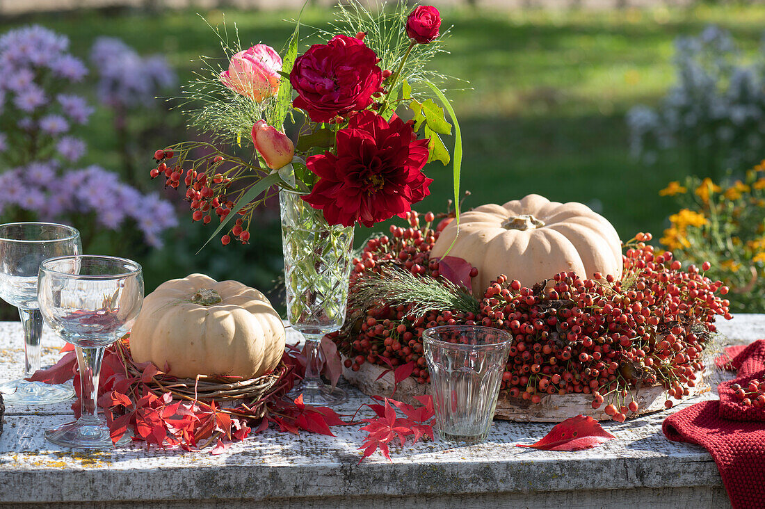 Herbstdekoration mit Mini-Muskat-Kürbis 'Butterkin' und Herbststrauß aus Rosen, Dahlie, Hexengras und Hagebutten, Kränze aus Hagebutten und wildem Wein