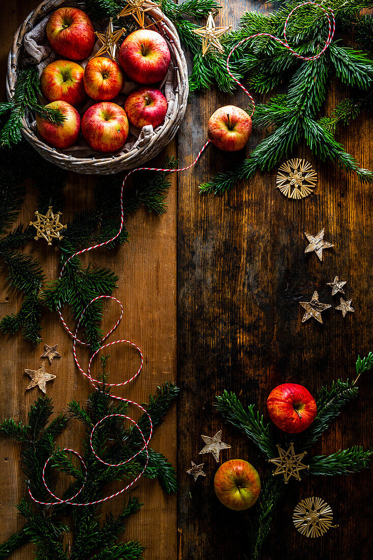 Weihnachtsdekoration mit Äpfeln, Tannenzweigen und Strohsternen auf Holzuntergrund