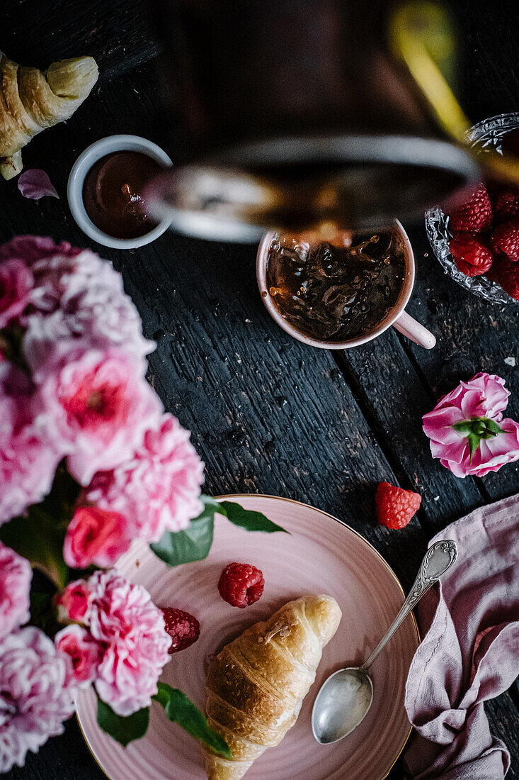 A breakfast table with croissants, raspberries and coffee