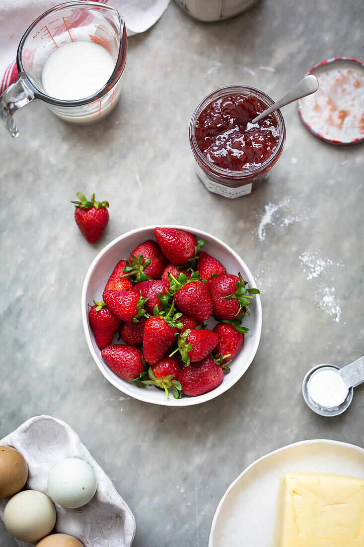 Schüssel mit Erdbeeren, Erdbeermarmelade, Milch, Butter und Eier