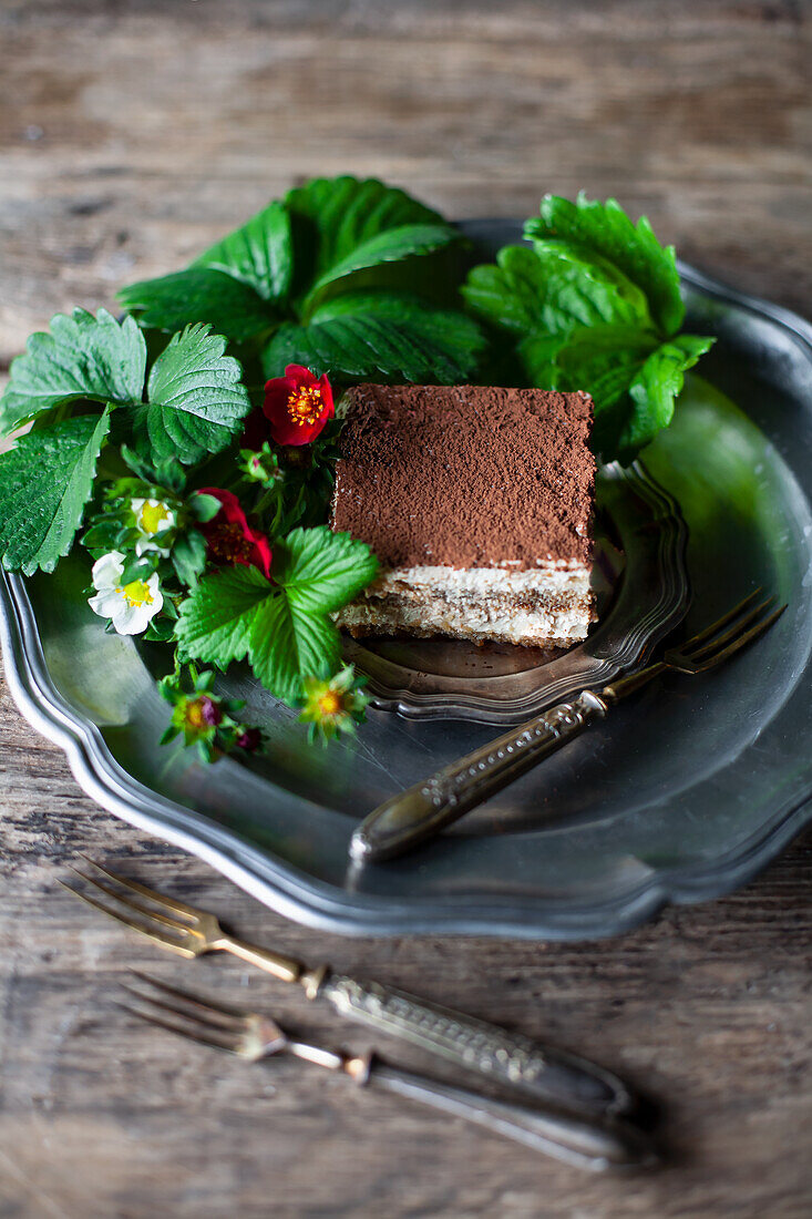 Tiramisu umgeben von Erdbeerblättern und Blüten