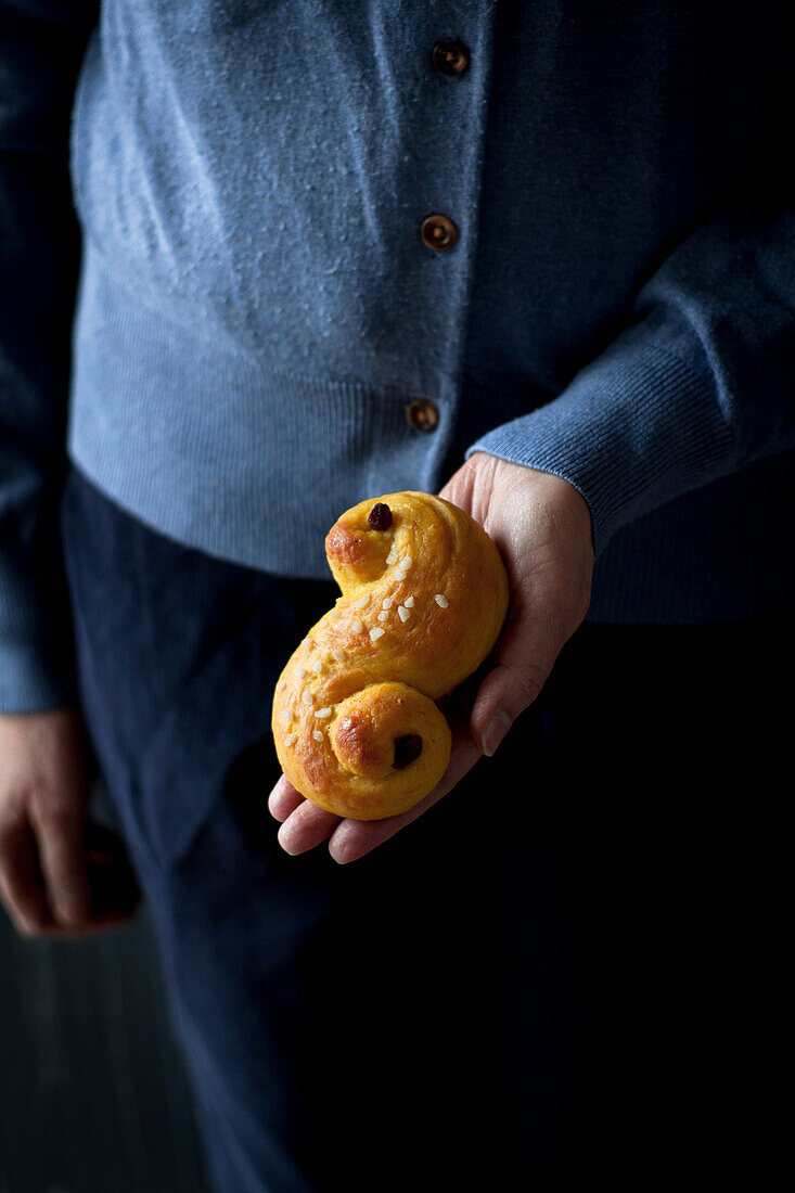 Hand hält Lussekatter (Schwedisches Hefegebäck)