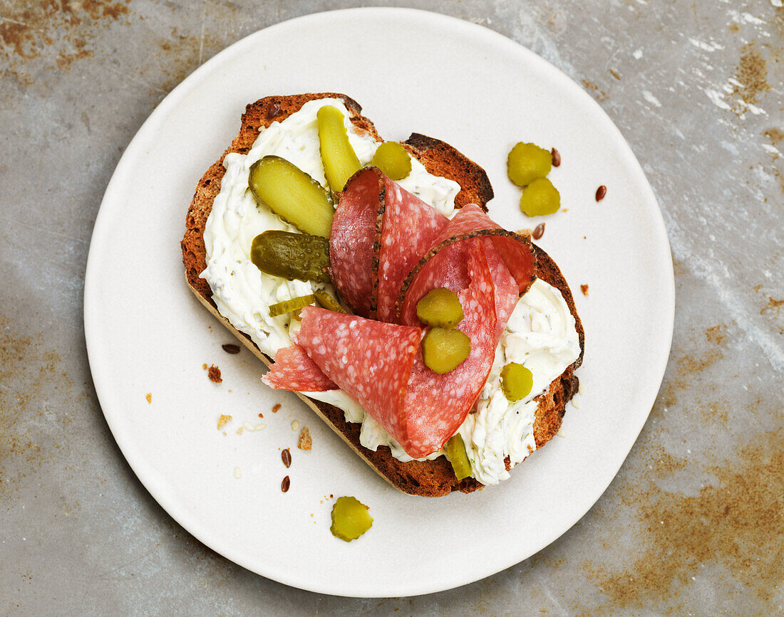 Open faced sandwich with cream cheese, salami, and pickles