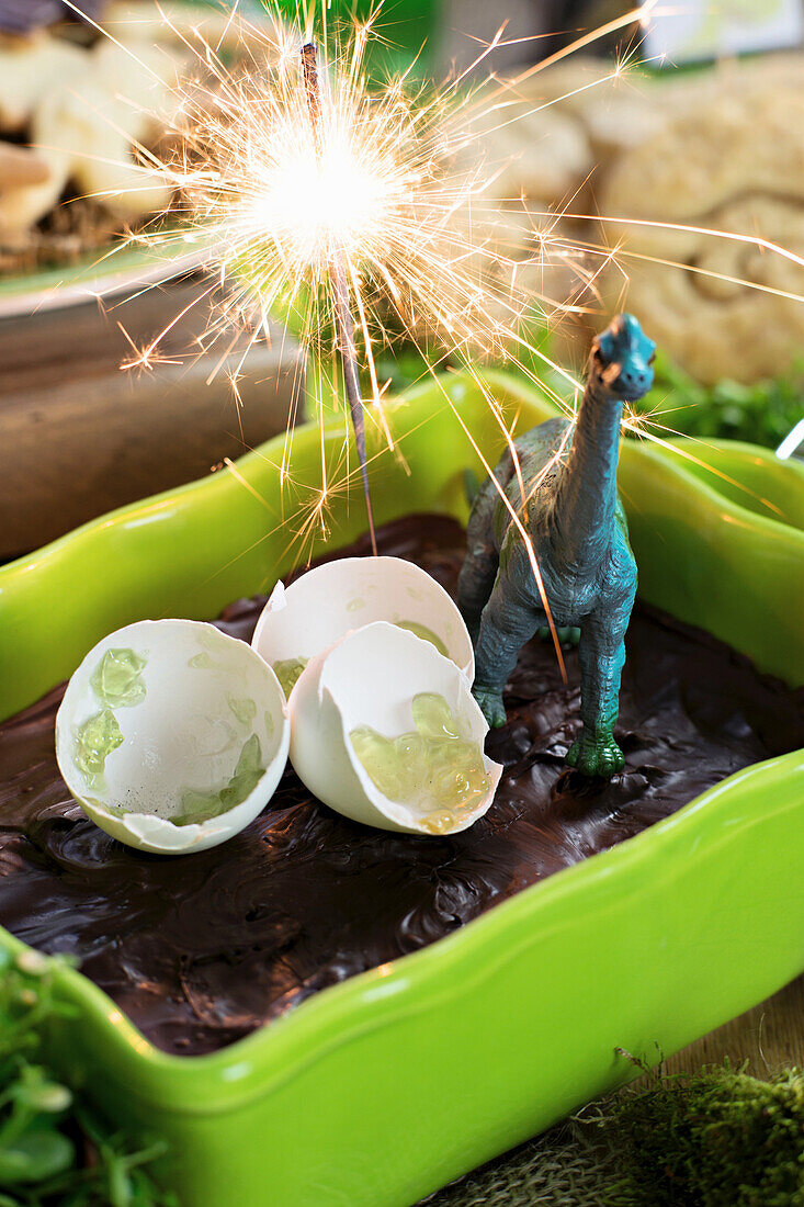 A chocolate cake with a sparkler, eggshells and a dinosaur figurine