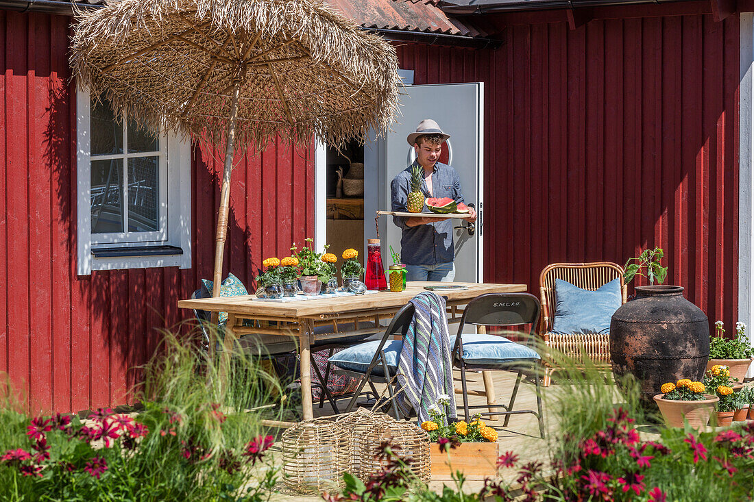 Terrasse mit Bambusmöbeln vor Holzhaus, Mann im Hintergrund