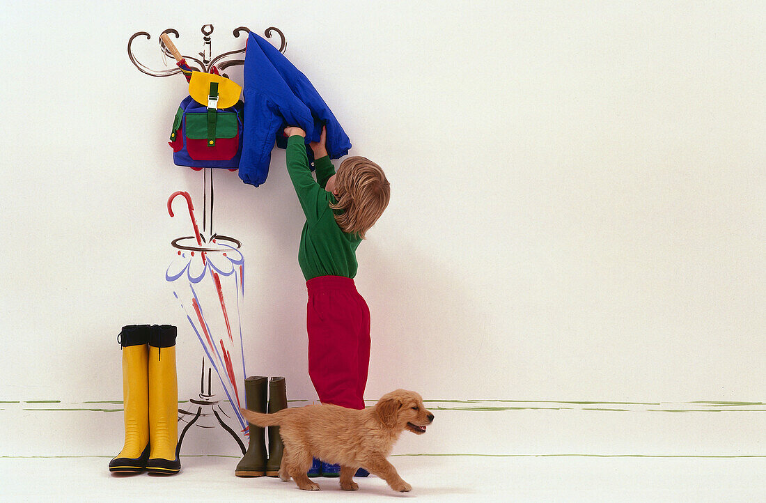 Boy reaching up to hang coat on coat stand