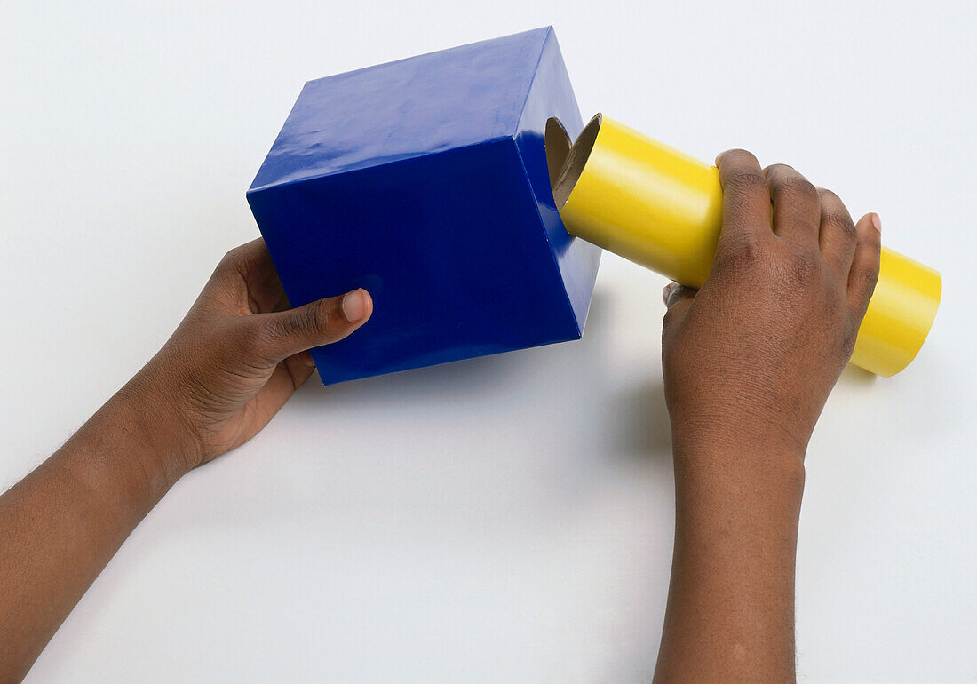 Child's hands pushing tube into hole in box