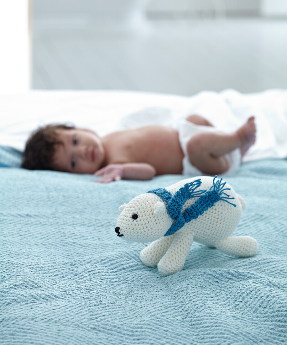 Baby lying on bed looking towards crocheted polar bear