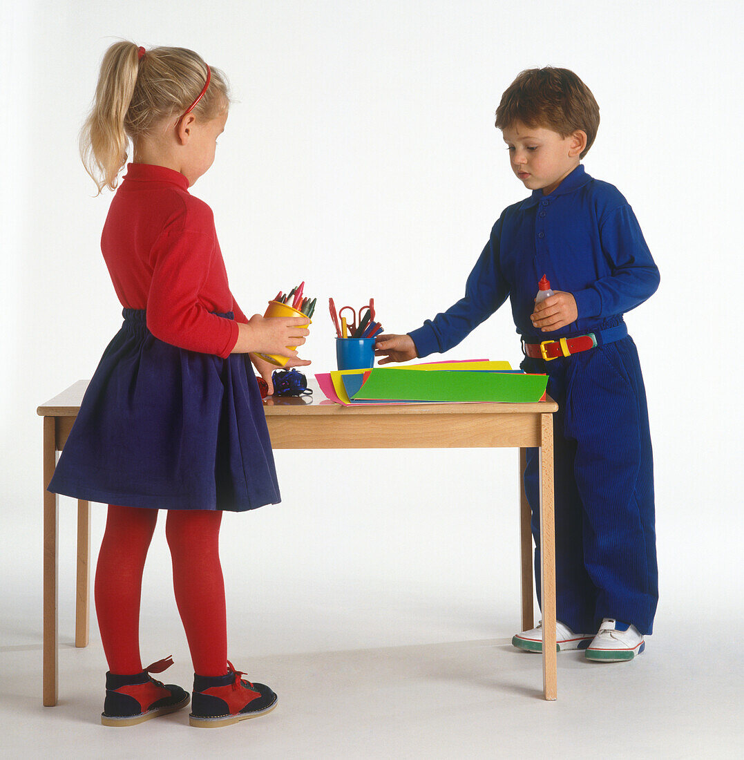 Boy and girl picking up writing tools from table