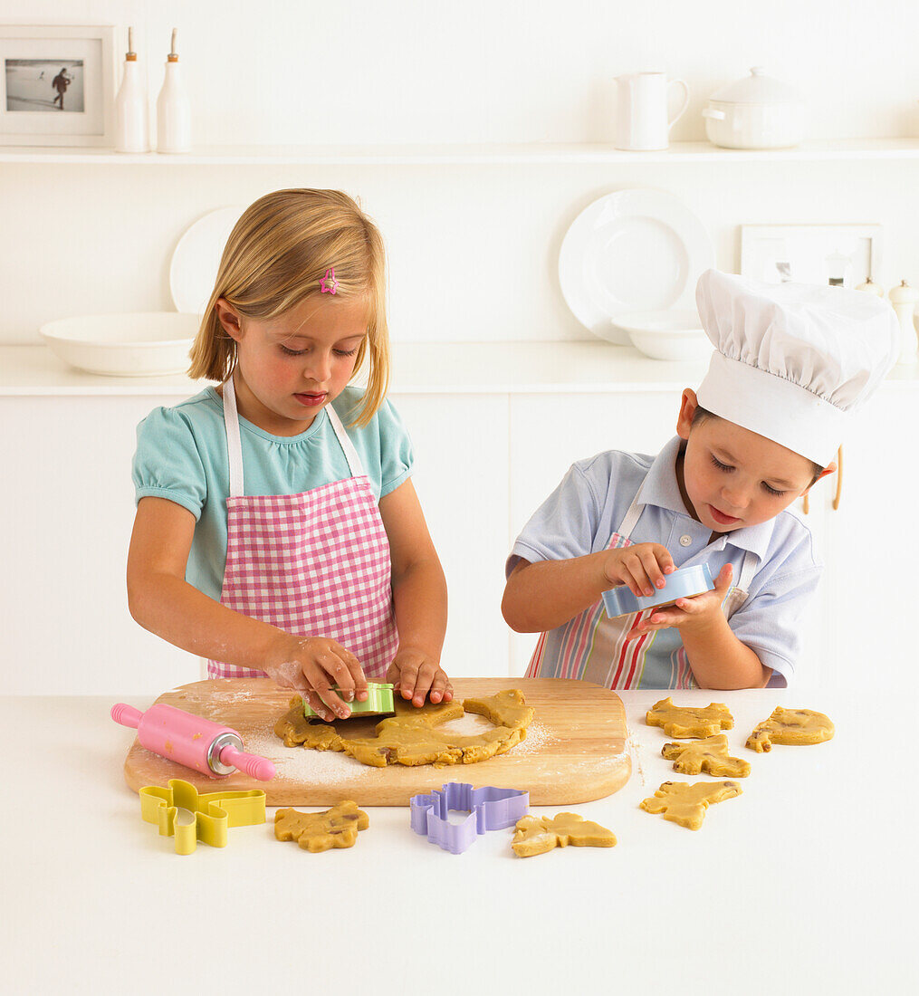 Boy and girl cutting shapes from dough using pastry cutters
