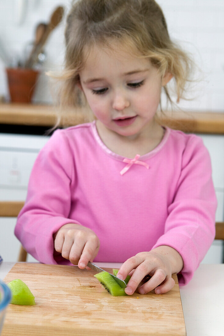 Girl slicing peeled kiwi fruit with knife