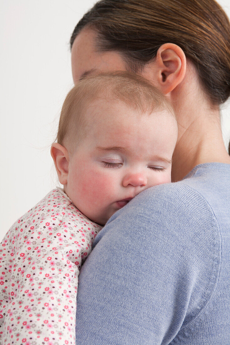 Mother holding sleeping baby girl against one shoulder