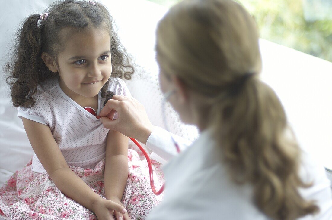 Doctor holding stethoscope to girl's chest