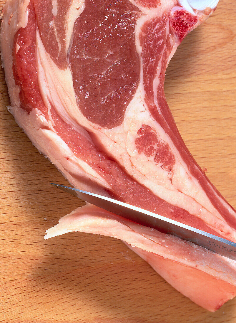 Slicing excess fat from a lamb chop with a chef's knife