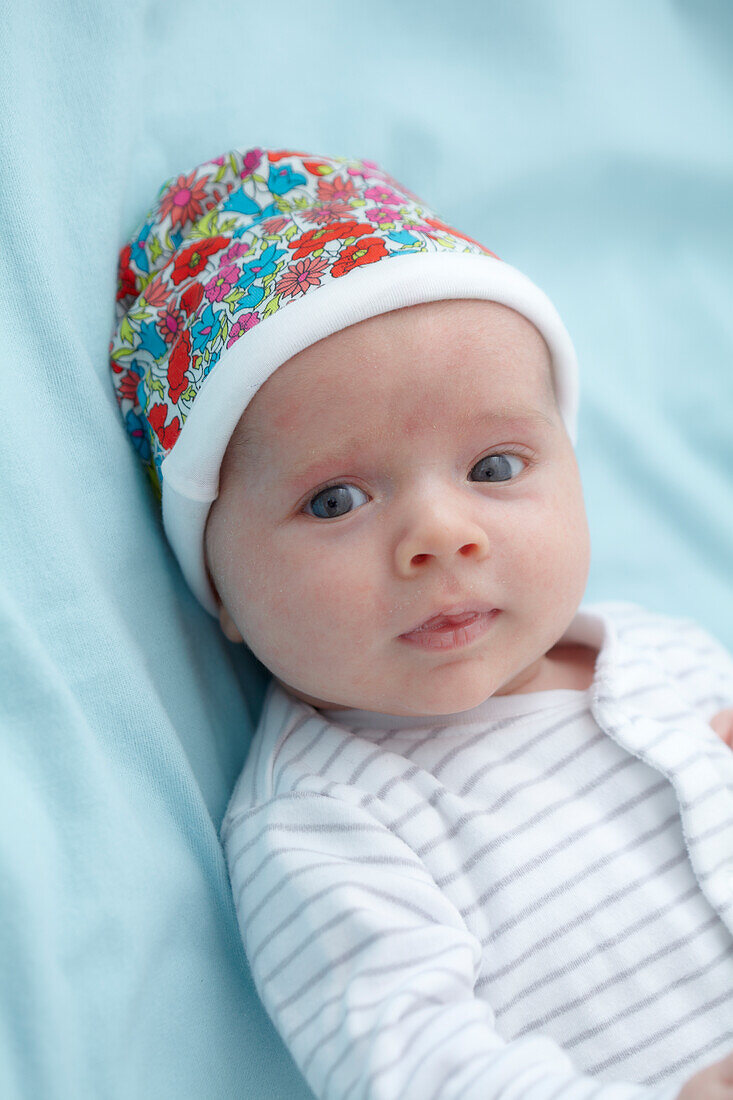 Baby boy lying down wearing a colourful cap