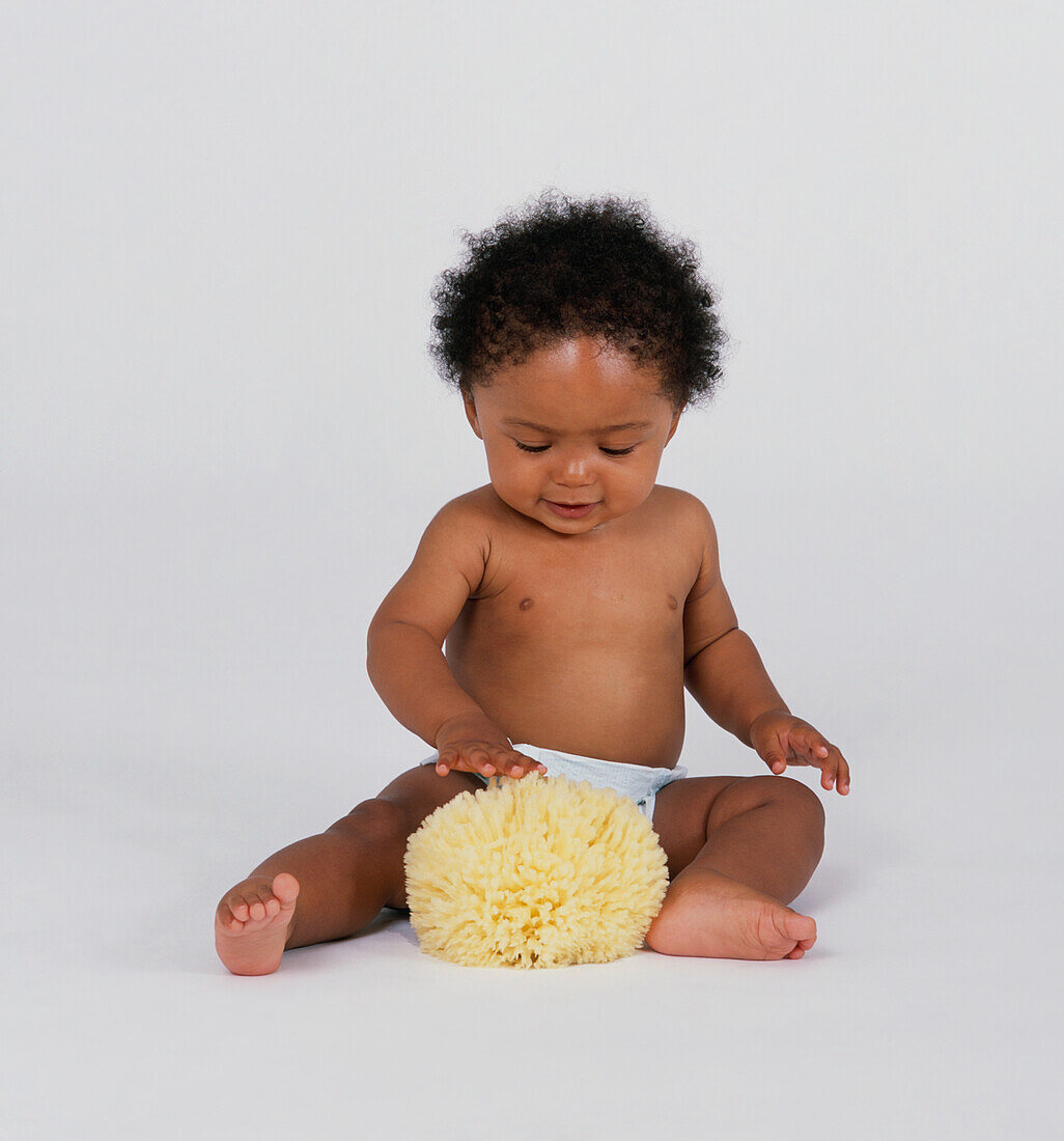 Baby boy sitting on floor touching natural sponge
