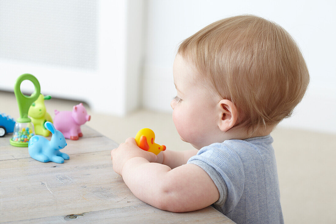 Baby boy looking at selection of plastic toys on table