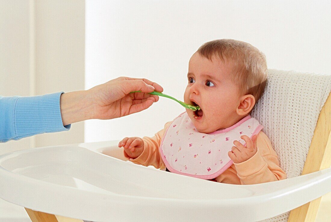 Baby in high chair being fed from spoon