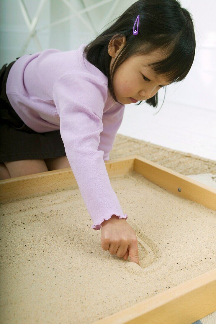 Girl drawing letter in sand with finger