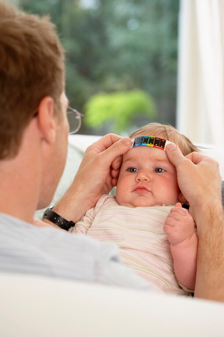 Man placing strip thermometer on baby girl's forehead