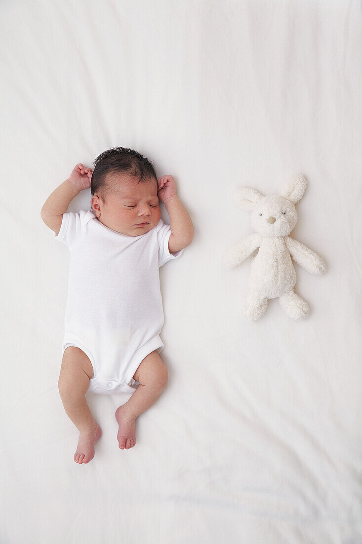 Baby girl lying next to a white bunny teddy