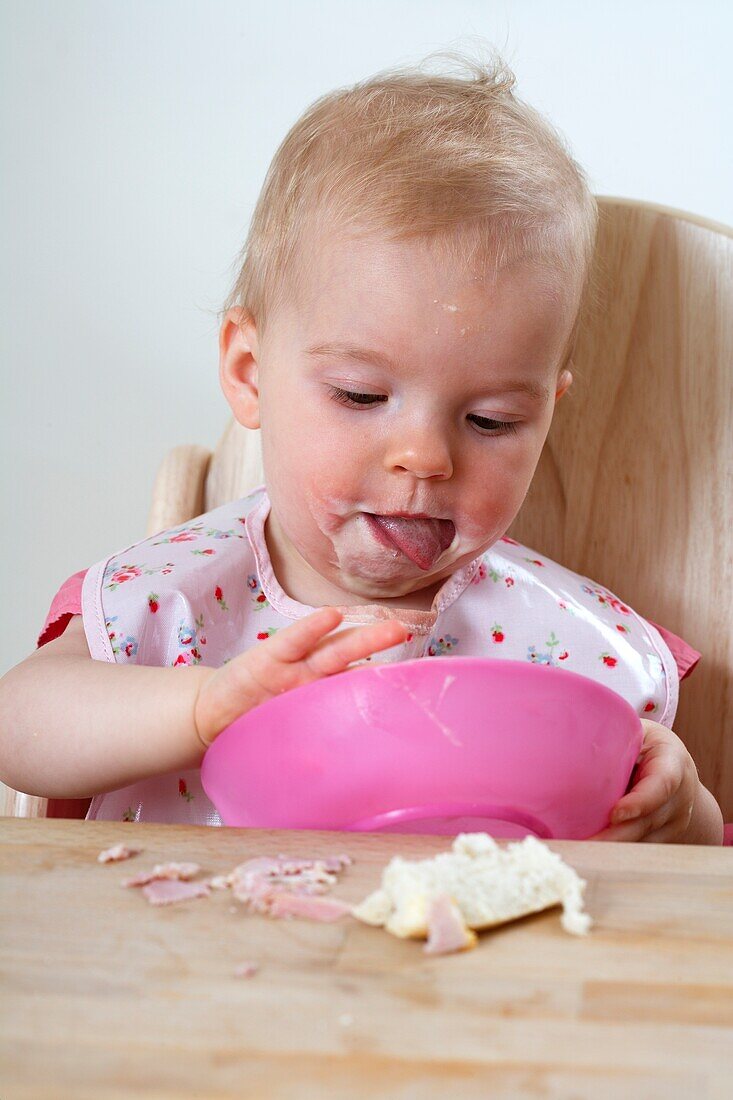 Baby girl in high chair eating from bowl using her hands