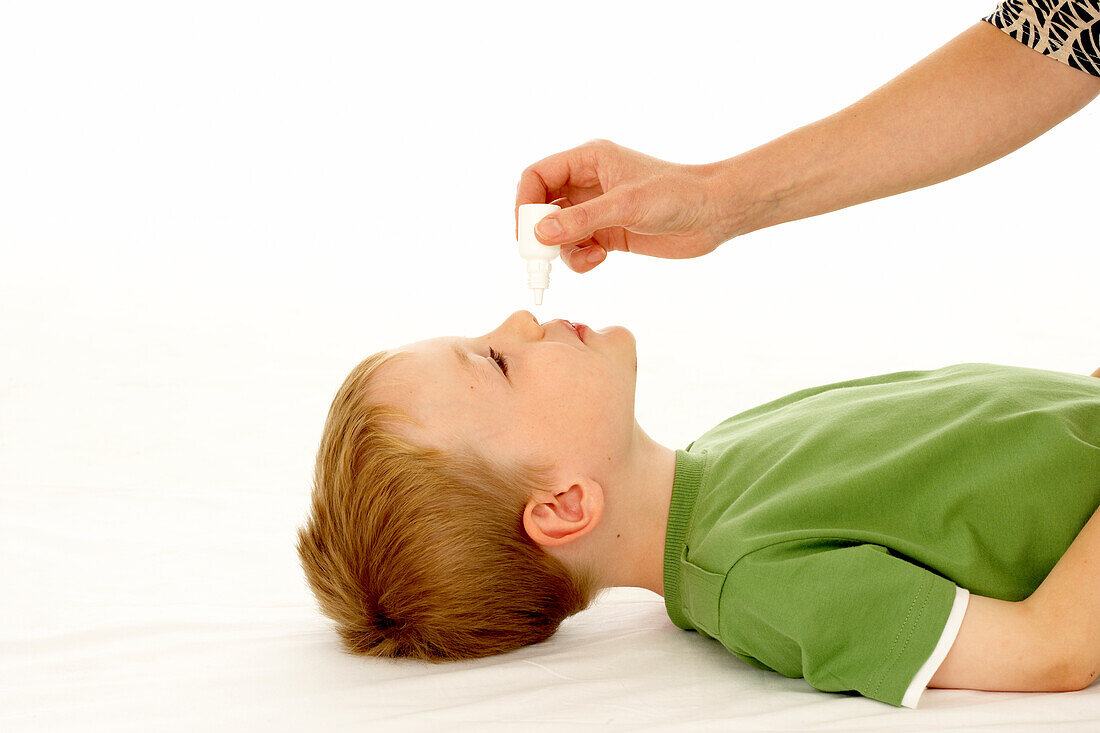 Boy lying down having drops applied into nose by woman